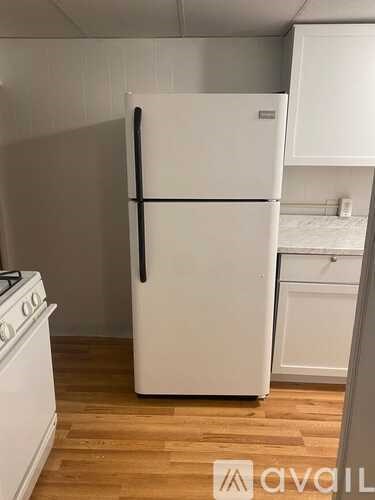A white refrigerator in a kitchen with wooden floors.