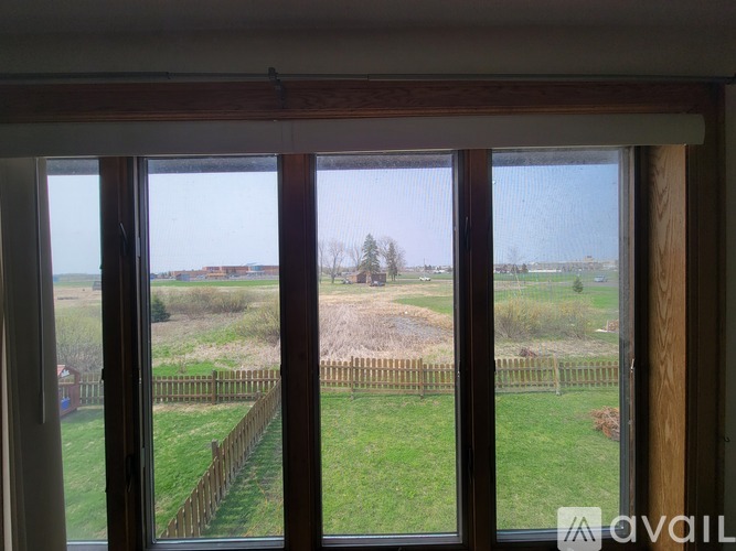 A view from a window looking out to a grassy field and a wooden fence.