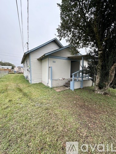 A small house with a blue door is surrounded by grass and trees.