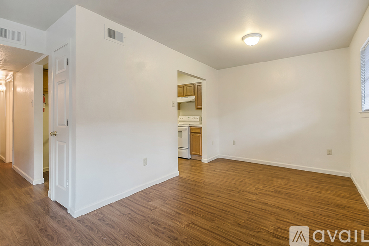 A room with wooden floors and white walls, with a doorway leading to another room.