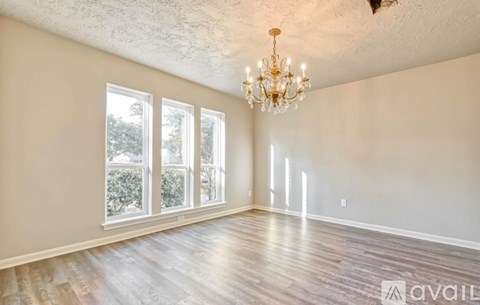 A room with a chandelier, hardwood floors, and three windows.