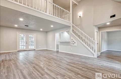 A spacious room with wooden flooring and a staircase with white railings.