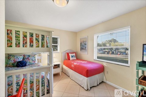 A bedroom with a red bed and a television on a stand.