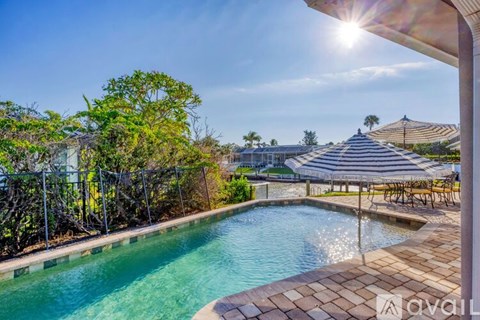 A pool surrounded by a patio and trees with a sunny sky.
