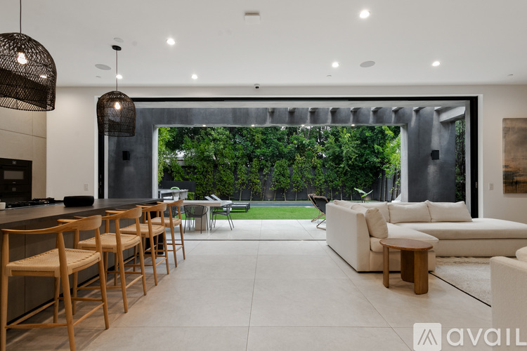 A modern kitchen with wooden chairs and a large window overlooking a green garden.