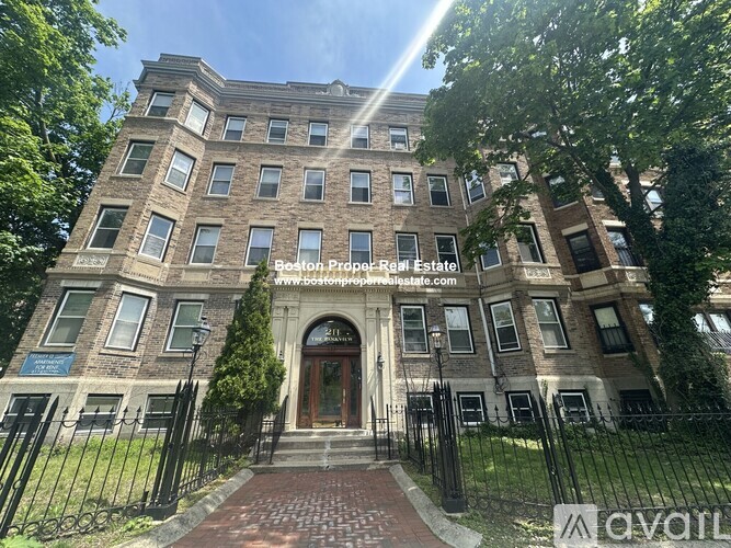 A large, multi-story building with a brick facade and a black metal fence in front.