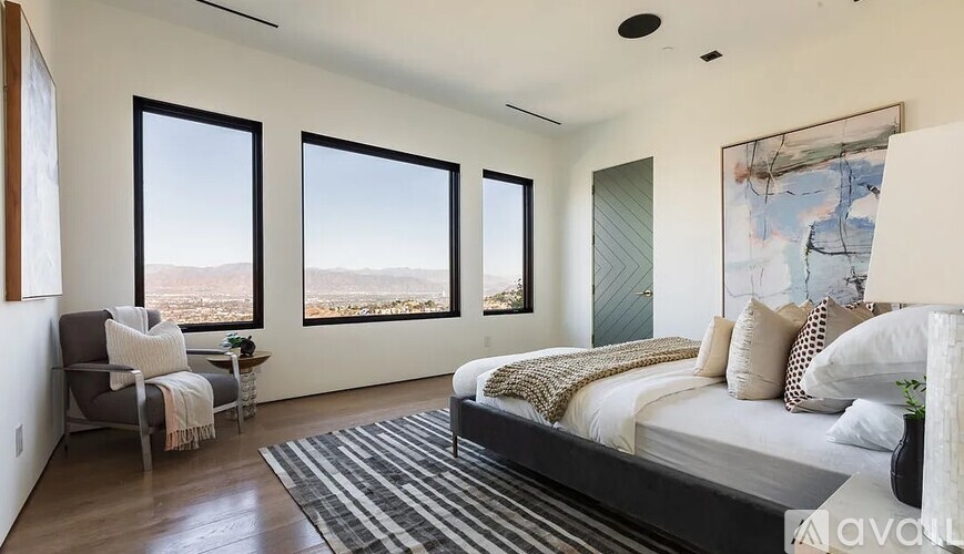 A bedroom with a large bed and a view of the outdoors through the windows.
