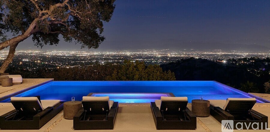 A pool with lounge chairs and a view of the city at night.