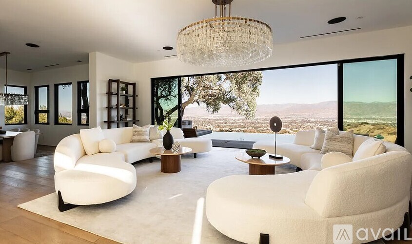 A living room with white furniture and a large window overlooking a valley.