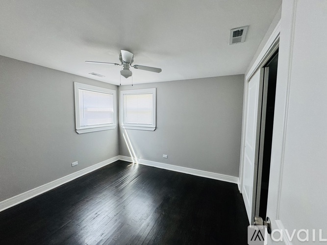 A room with a ceiling fan and two windows.