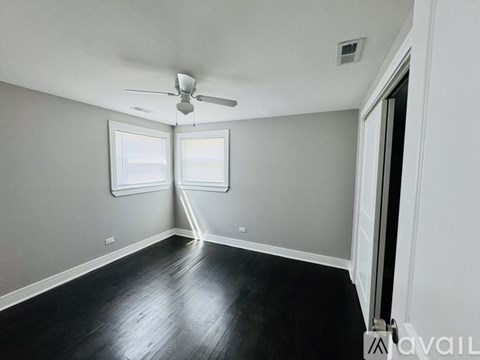 A room with a ceiling fan and two windows.
