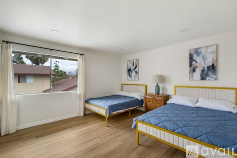 A bedroom with two beds and a window overlooking a residential area.