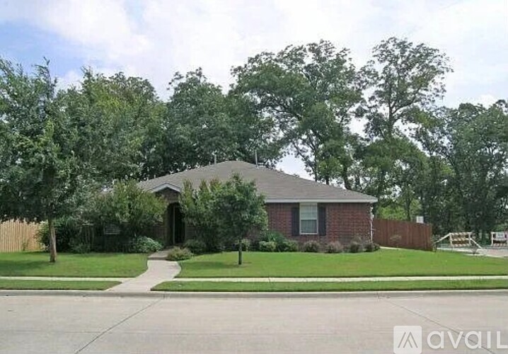 A house with a brown roof and a white fence is surrounded by green trees.