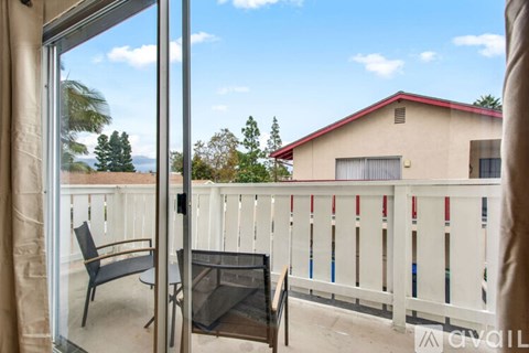 A balcony with a table and chairs overlooks a house and trees.