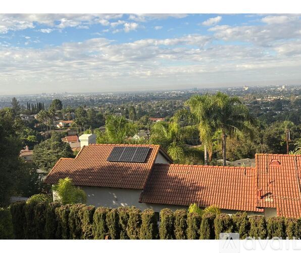 A house with a red tiled roof and solar panels on the roof is surrounded by green trees.
