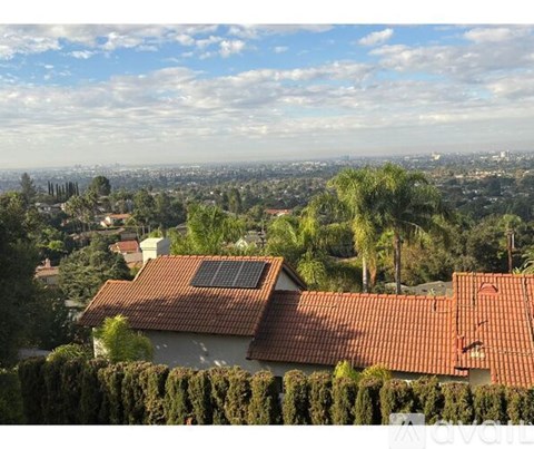 A house with a red tiled roof and solar panels on the roof is surrounded by green trees.