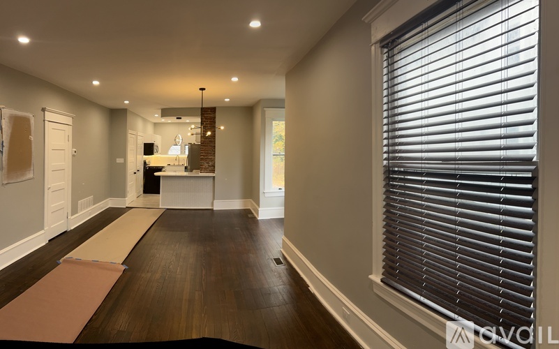 A long hallway with a rug on the floor and a window with blinds on the right side.