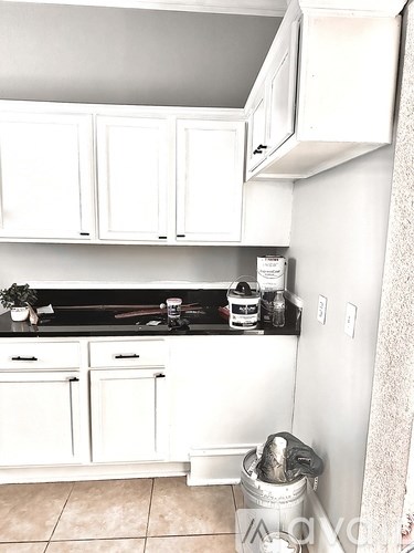 A kitchen with white cabinets and a black counter top.