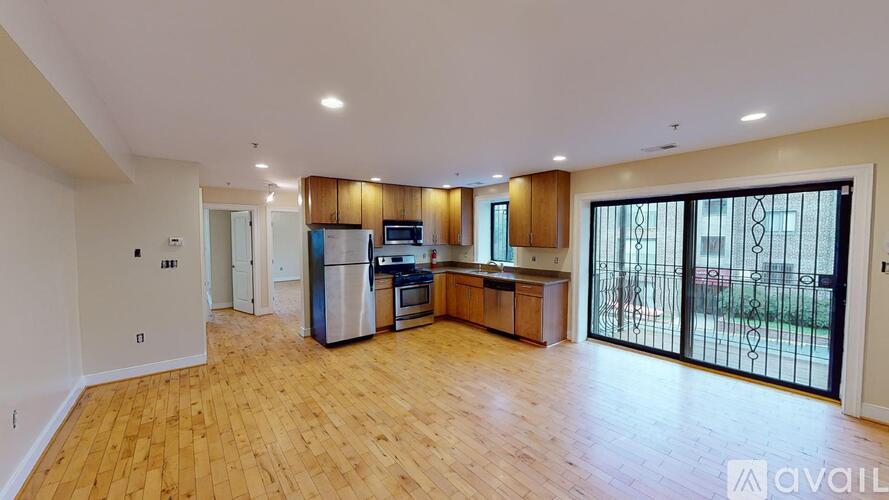 A spacious living room with wooden flooring and a kitchen area with stainless steel appliances.