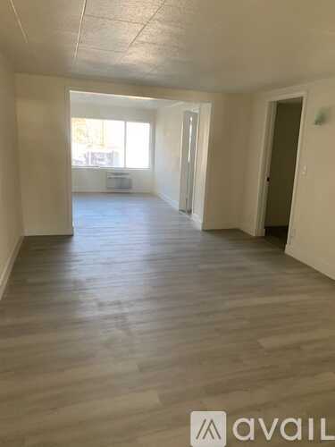 A spacious room with wooden flooring and white walls.