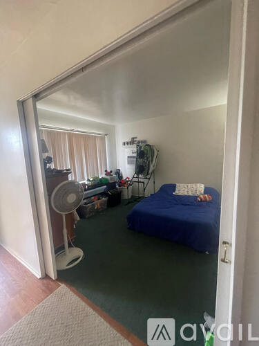 A bedroom with a bed, a fan, and a chair.