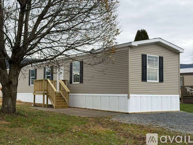 A mobile home with a deck and a tree in front.