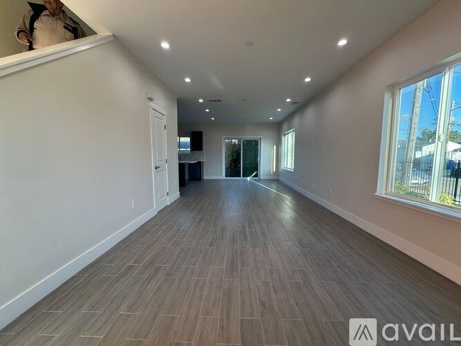 A spacious room with wooden flooring and a large window on the right side.