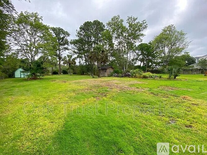A grassy field with trees and a house in the background.