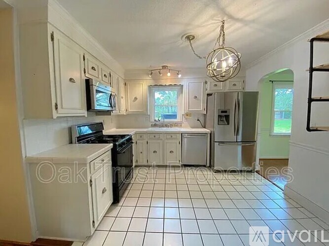 A kitchen with white cabinets and appliances, a black stove, and a white tiled floor.