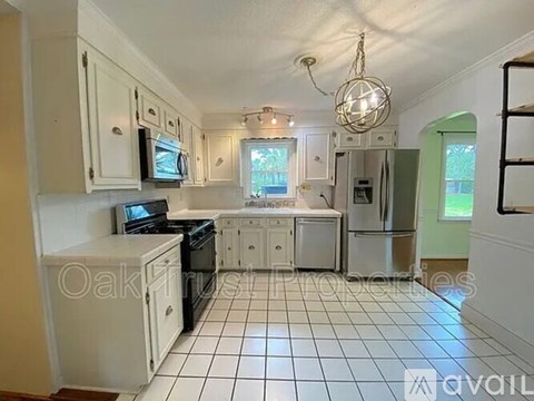 A kitchen with white cabinets and appliances, a black stove, and a white tiled floor.