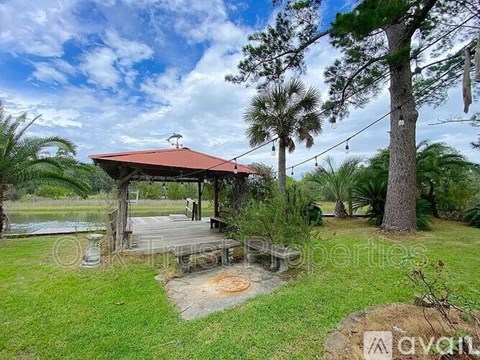 A gazebo is situated in a grassy area with a pond and trees in the background.