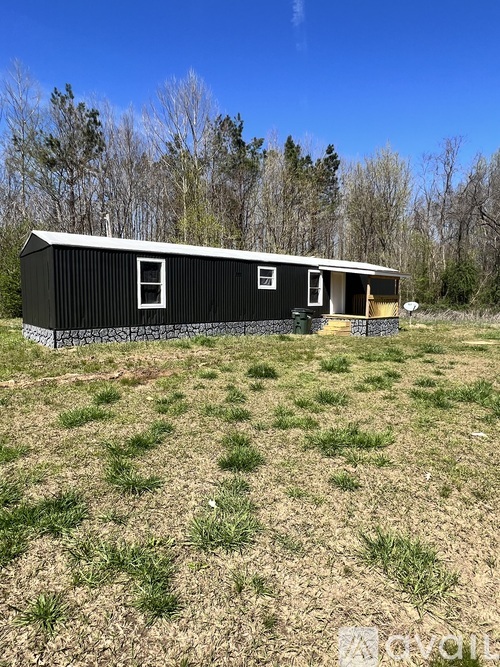 A black metal building with a white door and windows sits in a grassy field.