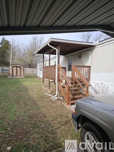 A carport with a wooden staircase leading to a white building.