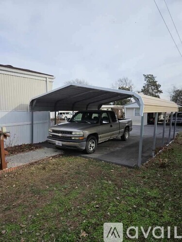 A silver truck is parked under a metal carport.