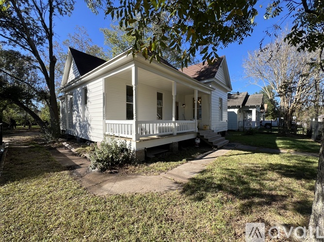 A white house with a porch and a tree in front.