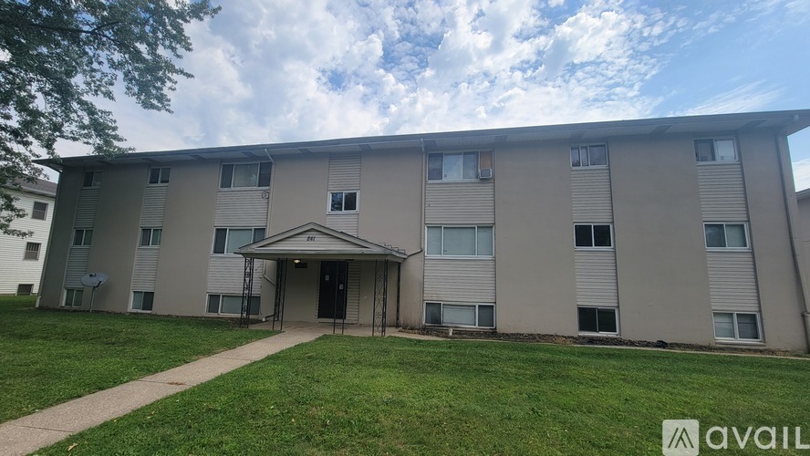 Apartment building with a grassy area in front and a cloudy sky above.