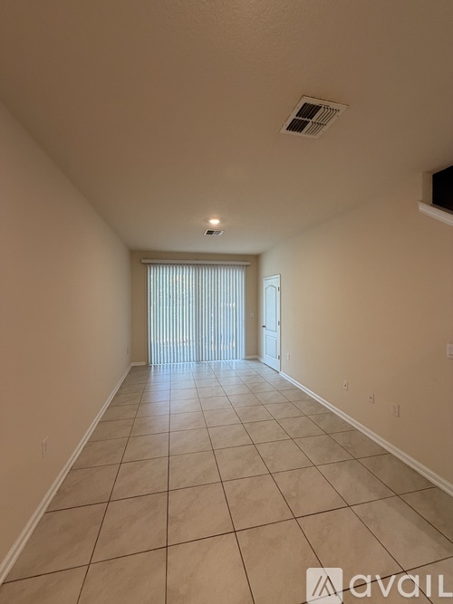 A long hallway with tiled floors and a window with blinds.