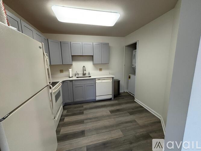 A kitchen with a white fridge, grey cabinets and a wooden floor.