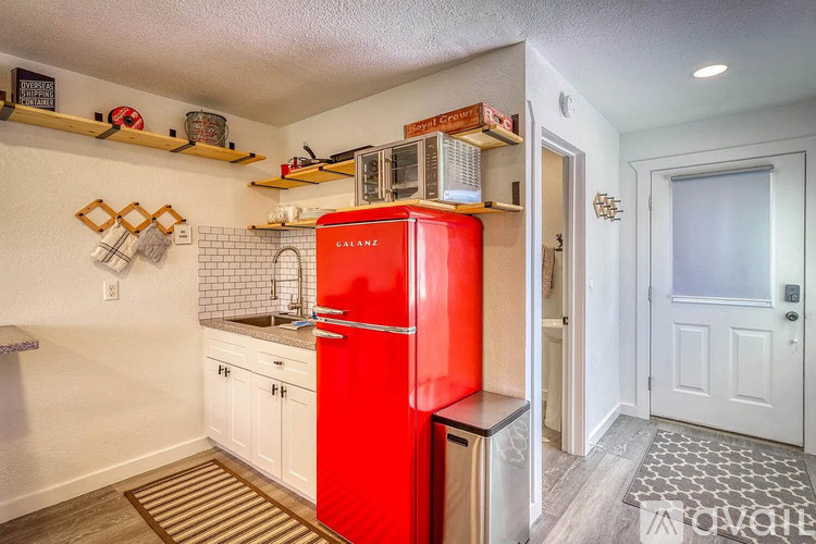 A red fridge in a kitchen with white cabinets and a white door.