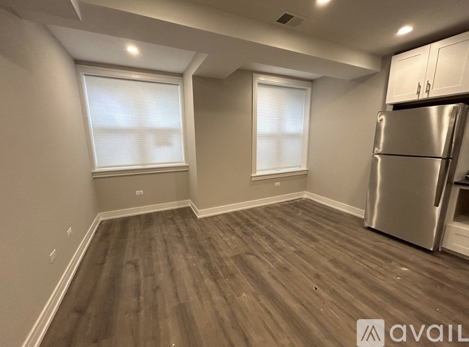 A kitchen with a refrigerator, wooden flooring, and two windows.
