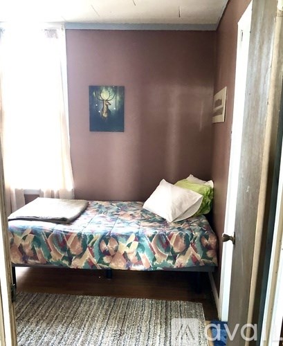 A bed with a floral patterned cover sits in a room with a painting on the wall.