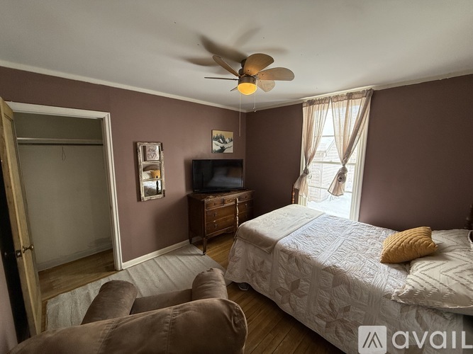 A bedroom with a bed, chair, and a ceiling fan.