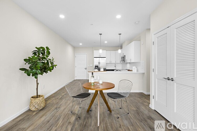 A room with a round table and chairs, a potted plant, and a kitchen area in the background.