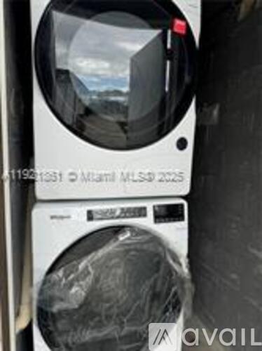 A washing machine is wrapped in plastic and has a sticker on it that reads "11996153 Miami MLS# 2025".