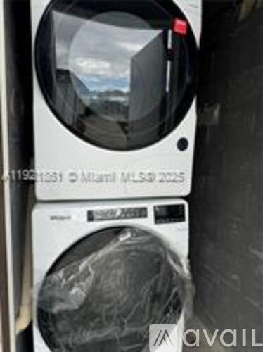 A washing machine is wrapped in plastic and has a sticker on it that reads "11996153 Miami MLS# 2025".