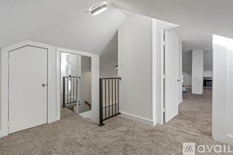 A spacious room with a carpeted floor and a staircase with a black railing.