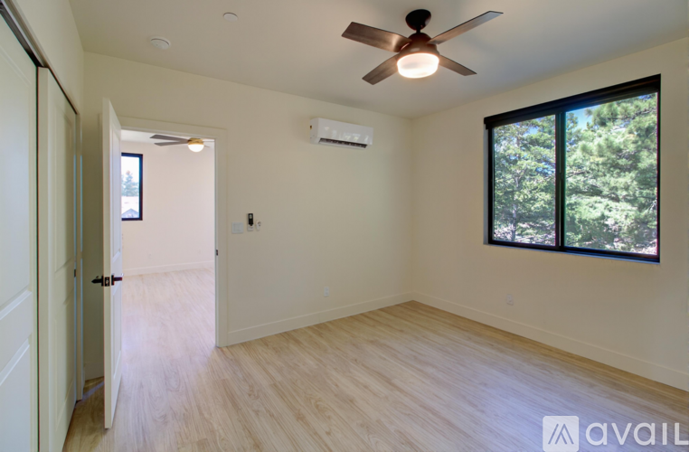 A room with a ceiling fan and a window with a view of trees.