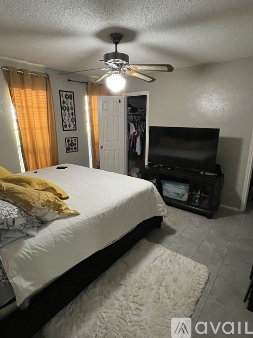 A bedroom with a bed, a ceiling fan, and a TV in the corner.
