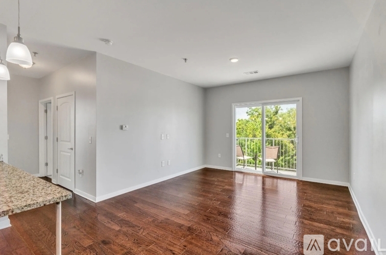 A spacious room with wooden floors and a sliding glass door leading to a balcony.