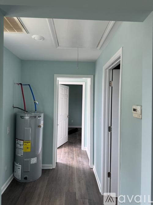 A long hallway with a grey water heater on the left and a door on the right.